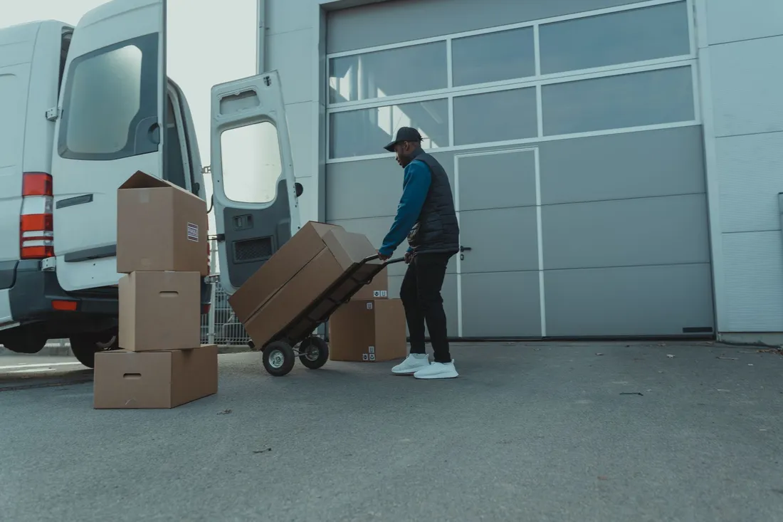 Arbeiter mit Sackkarre und Kartons am offenen Transporter vor dem Hallentor