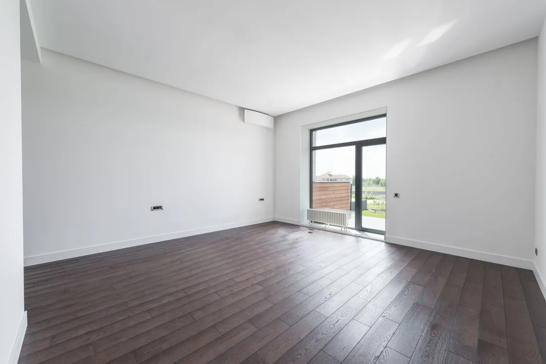 Vollständig leerer Wohnraum mit dunklem Dielenboden und bodentiefem Fenster nach der Räumung