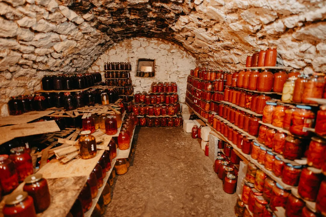Alter Gewölbekeller mit Holzregalen voller eingemachter Gläser im warmen, gedämpften Licht