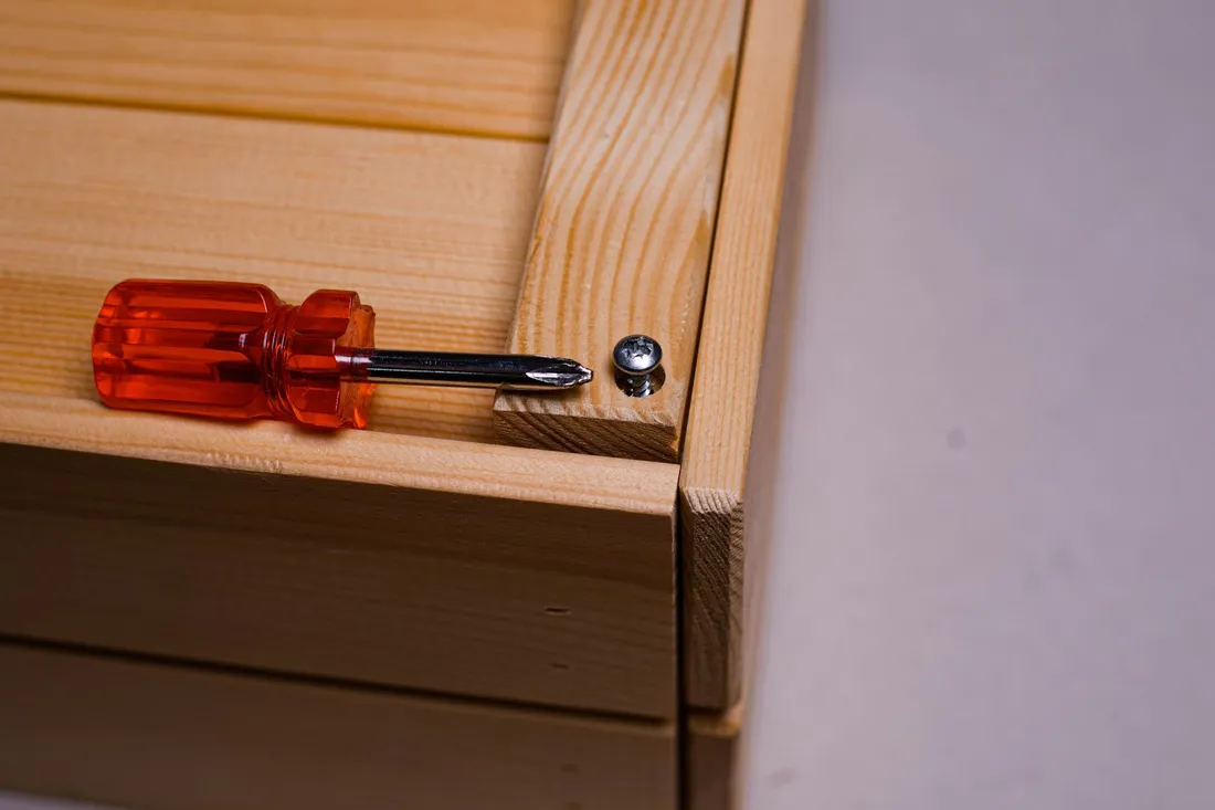 Roter Schraubendreher und eine Schraube liegen auf einem unlackierten Holzmöbel während der Montage