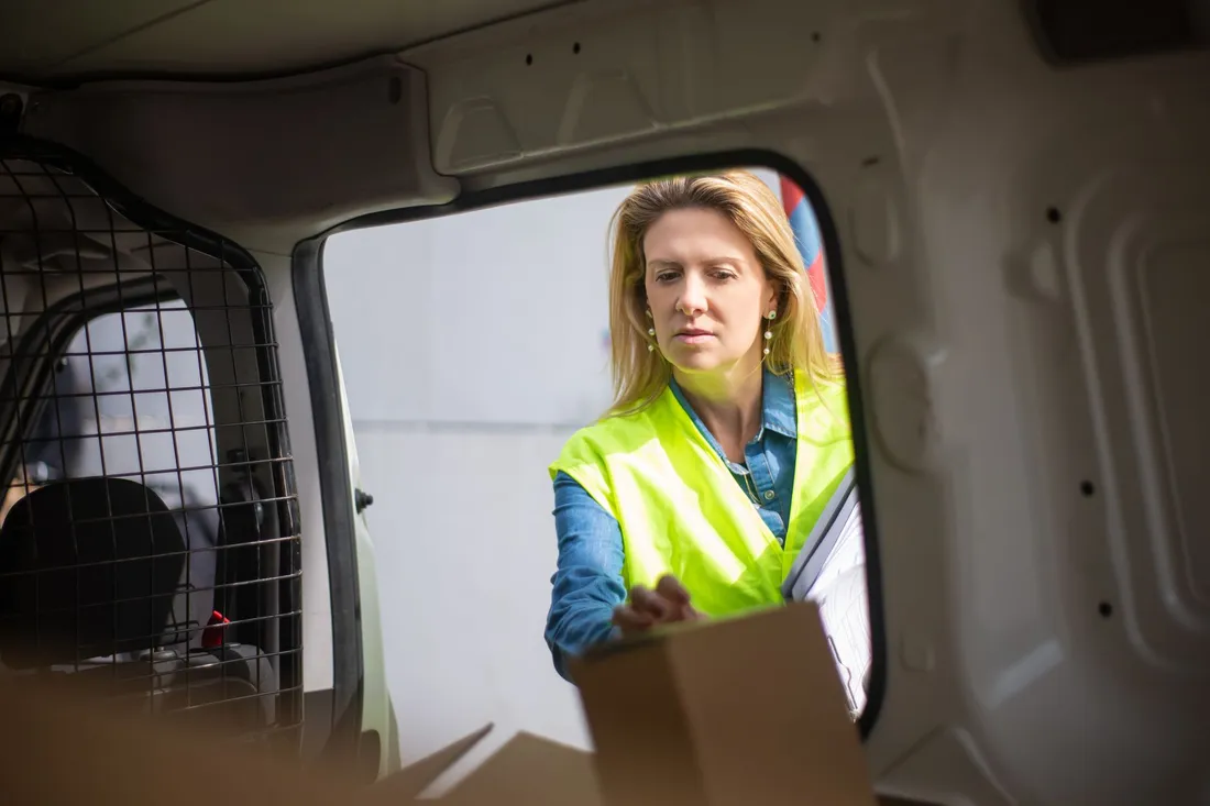 Blick aus dem halb leeren Laderaum eines Transporters auf eine Helferin in Warnweste mit Karton